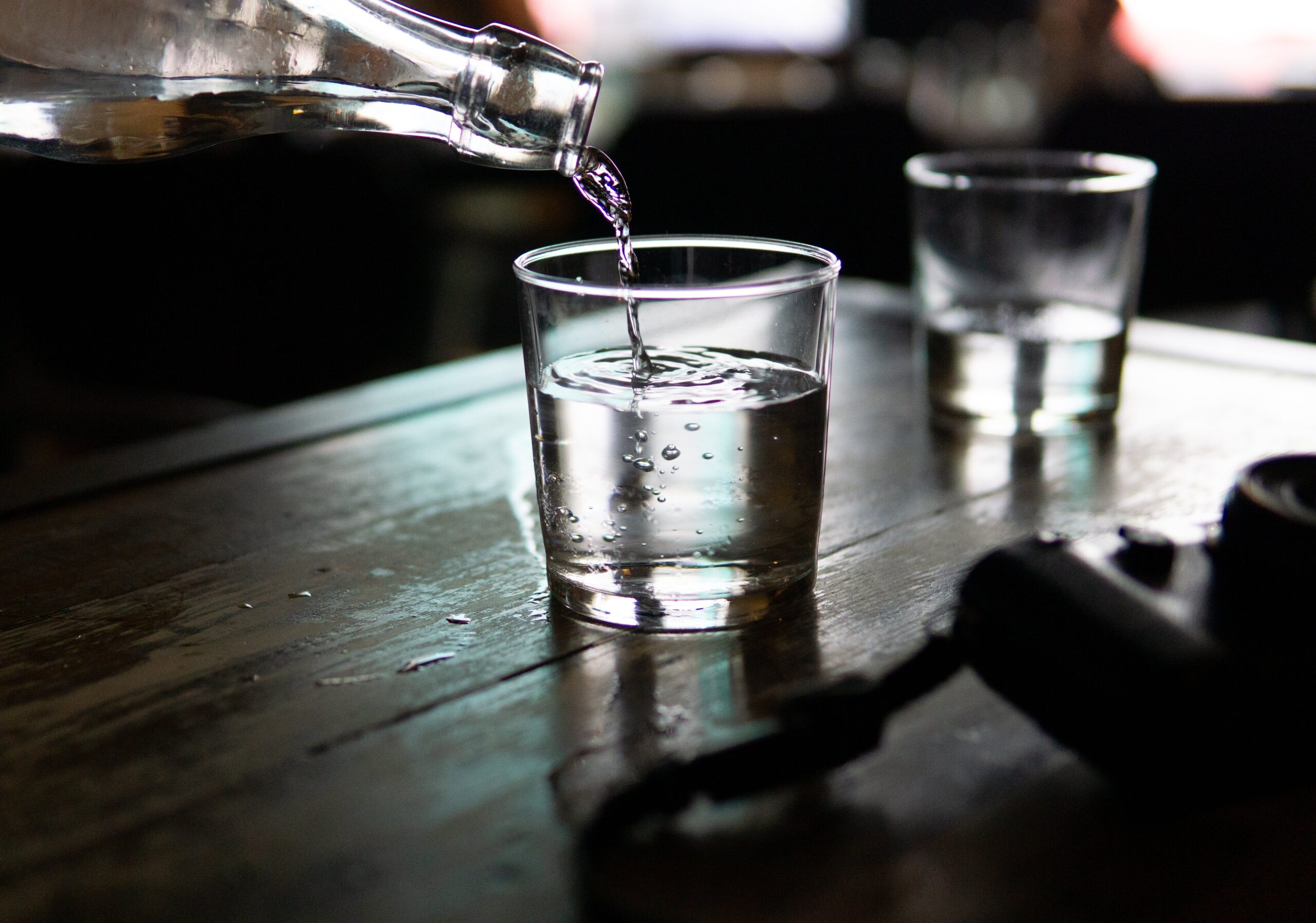 Clear Drinking Glass on a wooden table being filled with water from a clear bottle