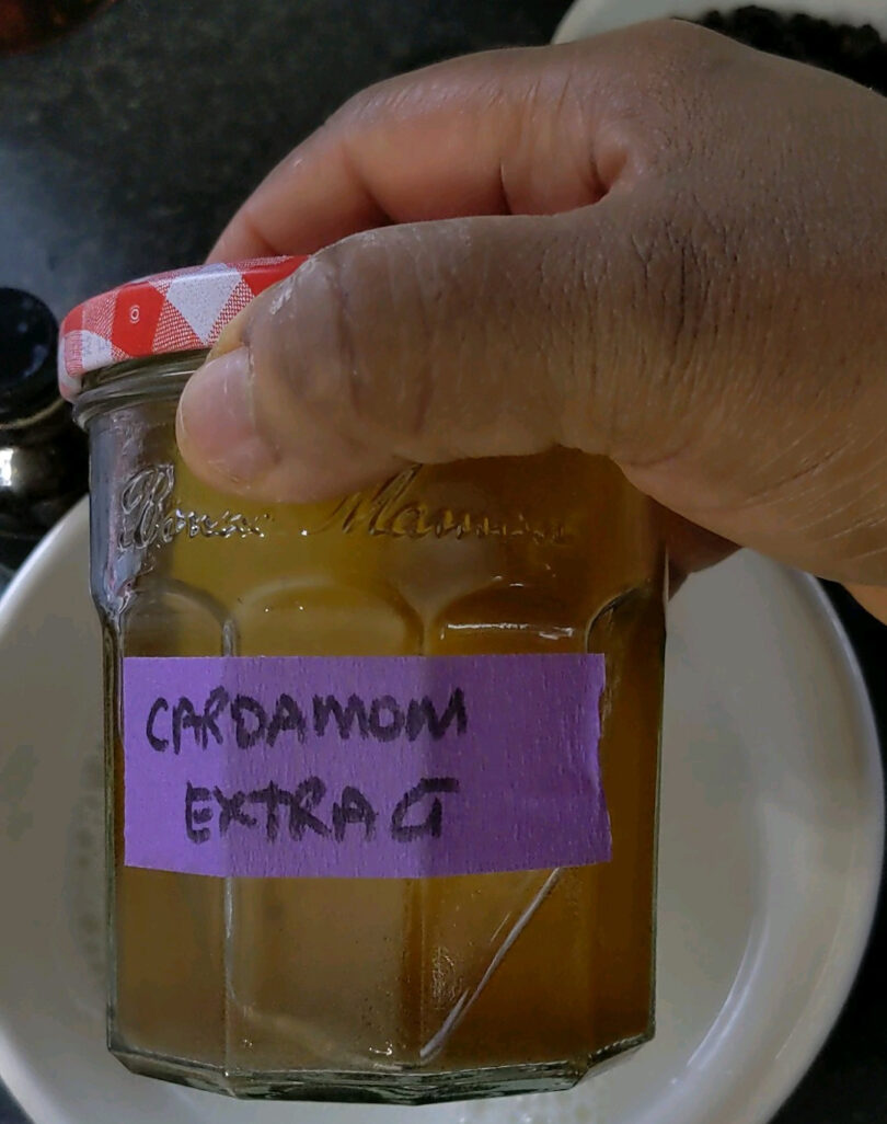 Red gingham lid on glass jar labelled, on purple painter's tape, cardamom extract